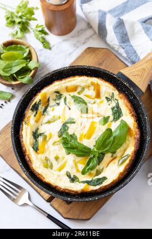 Spinat und Käseomelett. Frittata aus Eiern, Paprika und Spinat in einer Pfanne auf einer Marmorplatte. Stockfoto