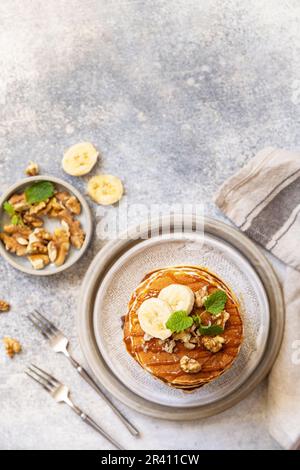 Zum Feiern des Pfannkuchen-Tages, amerikanisches hausgemachtes Frühstück. Glutenfreie Bananen-Pfannkuchen mit Nüssen und Karamell auf einer Tischplatte aus Stein. Anzeigen Stockfoto