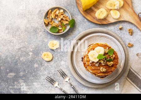 Zum Feiern des Pfannkuchen-Tages, amerikanisches hausgemachtes Frühstück. Glutenfreie Bananen-Pfannkuchen mit Nüssen und Karamell auf einer Tischplatte aus Stein. Anzeigen Stockfoto