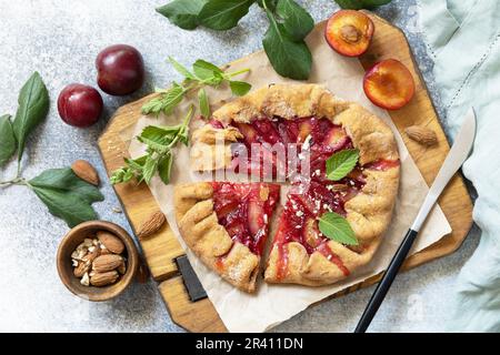 Plum Galette. Gesunder hausgemachter Vollkornfruchtkuchen (Galette) mit Pflaumen und Mandeln, veganes vegetarisches Dessert auf einem Steintisch. Stockfoto