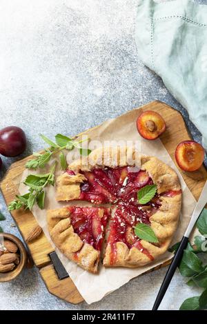 Plum Galette. Gesunder hausgemachter Vollkornfruchtkuchen (Galette) mit Pflaumen und Mandeln, veganes vegetarisches Dessert auf einem Steintisch. Stockfoto