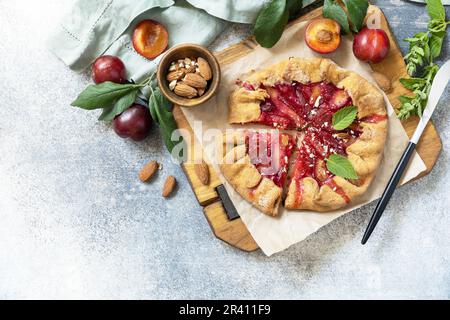 Plum Galette. Gesunder hausgemachter Vollkornfruchtkuchen (Galette) mit Pflaumen und Mandeln, veganes vegetarisches Dessert auf einem Steintisch. Stockfoto
