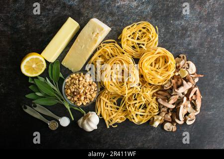 Tagliatelle mit Pilzen, Salatbutter und gerösteten Haselnüssen Zutaten: Blick von oben auf Nudelnester mit Pilzen, Kräutern und anderen Zutaten Stockfoto