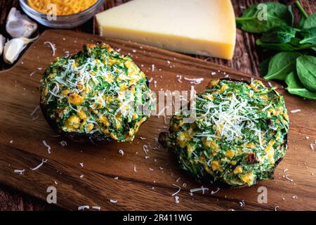 Mit Spinat und Käse gefüllte Pilze, garniert mit geriebenem Parmesan Reggiano: Zwei geröstete gefüllte portobello-Pilzkappen, von oben gesehen Stockfoto