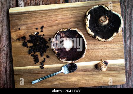 Reinigung und Stemmen eines Paars Portobello Pilzkappen: Die Kiemen von rohen Pilzkappen auf einem Holzbrett abkratzen Stockfoto