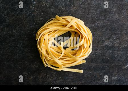 Ein einzelnes Tagliatelle Pasta Nest im dunklen Hintergrund: Ein Nudelnest aus getrockneten Nudeln, das aus nächster Nähe von oben betrachtet wird Stockfoto