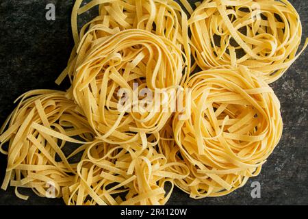 Tagliatelle Pasta Nester gestapelt und angesehen Nahaufnahme von oben: Nester aus getrockneten Nudelnudeln stapelten sich in einer Gruppe und blickten direkt von oben Stockfoto