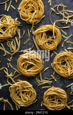 Tagliatelle Pasta Nester umgeben von verstreuten Nudeln: Mehrere getrocknete Nudelnester, die auf eine Küchenarbeitsfläche gelegt werden Stockfoto