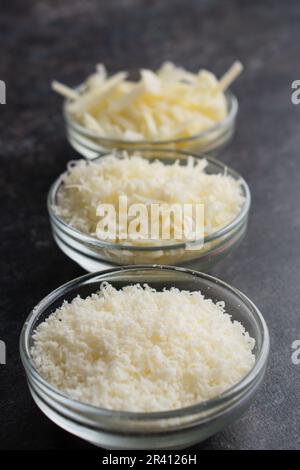 Frisch geriebener und geriebener Parmesankäse in Glasschüsseln: Drei verschiedene Texturen geriebener Parmesankäse mit der feinsten Konsistenz vorne Stockfoto