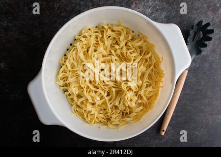 Gekochte Tagliatelle Pasta in einem großen Colander mit einem Pasta-Löffel: Frisch gekochte und abgetropfte Nudeln in einem großen Sieb mit einer Nudelgabel Stockfoto