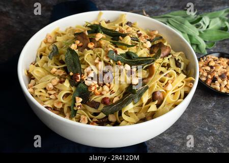 Tagliatelle mit Pilzen, Salbei-Butter und gerösteten Haselnüssen in einer Servierschüssel: Ein Blick aus der Nähe auf eine große Servierschale mit Nudeln Stockfoto