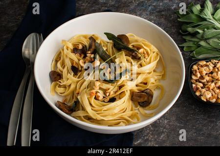 Tagliatelle mit Pilzen, Salbeibutter und gerösteten Haselnüssen in einer Pastaschale: Eine Portion Nudeln garniert mit gebratenen Salbeiblättern in einer flachen Schüssel Stockfoto