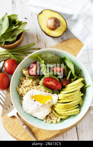 Köstliches Frühstück oder Brunch - pochiertes Ei, Quinoa, Avocado und frischer Gemüsesalat auf dem Küchentisch. Keto-Diät. Stockfoto