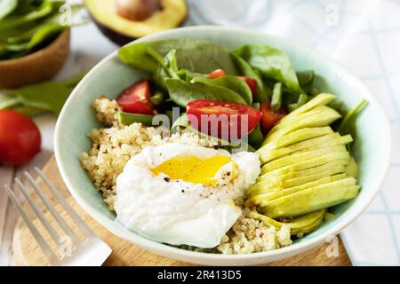 Keto-Diät. Köstliches Frühstück oder Brunch - pochiertes Ei, Quinoa, Avocado und frischer Gemüsesalat auf dem Küchentisch. Stockfoto