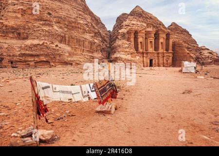 Souvenirteppiche, Teppiche und Schals sind neben dem Marktstand in Petra ausgestellt, mit Klosterbau im Hintergrund Stockfoto