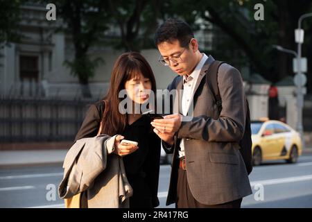 Ein asiatisches Paar stand mit Smartphones auf der Straße der Stadt im Hintergrund eines Taxifahrzeugs Stockfoto