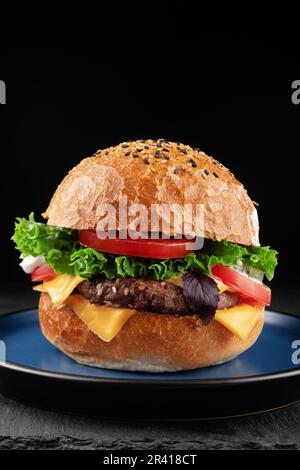 Hamburger mit Käse, Salat und Tomaten auf schwarzem Hintergrund. Stockfoto