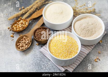 Lebensmittel und glutenfreie Backzutat. Getreide und Mehl grob, Maismehl, Buchweizenmehl, Kichererbsenmehl über grauem Stein Stockfoto