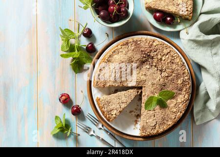 Hausgemachtes Sommergebäck, glutenfrei. Schokoladen- und Hüttenkäsekuchen mit Kirschen auf einem rustikalen Tisch. Blick von oben. Kopieren Sie Spac Stockfoto