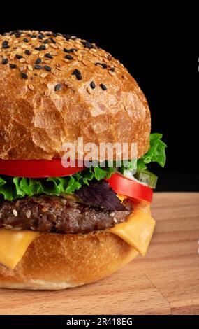 Nahaufnahme eines Burgers auf Holzschneidebrett mit schwarzem Hintergrund. Stockfoto