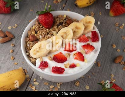 Joghurt mit Banane, Erdbeeren und Nüssen auf Holzhintergrund. Gesundes Frühstück. Stockfoto