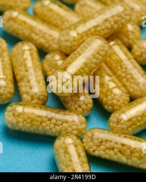 Transparente medizinische Kapseln mit gelbem Granulat innen auf blauem Hintergrund, Tabletten zur Behandlung, Vitamine Stockfoto