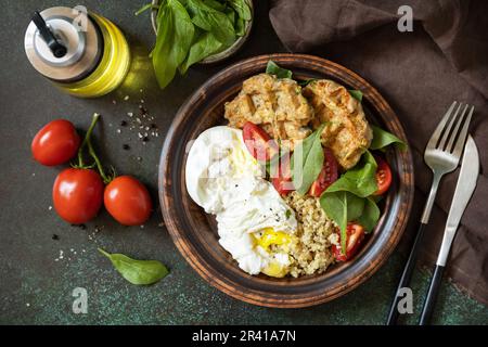 Keto-Diät. Köstliches Frühstück oder Brunch - vegane Zucchini-Waffeln, pochiertes Ei, Quinoa und frischer Gemüsesalat auf einem Steintisch Stockfoto