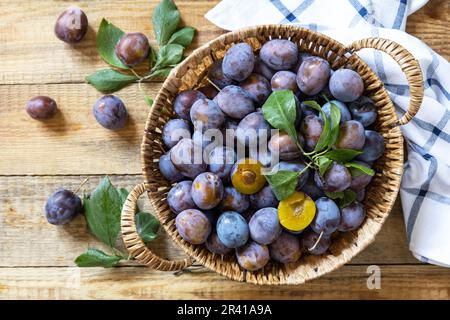 Obst Hintergrund, Bio-Früchte. Stillleben Essen. Korb mit frischen blauen Pflaumen auf einem rustikalen Holztisch. Blick von oben. Stockfoto