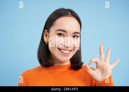 Nahaufnahme des Porträts einer lächelnden, wunderschönen asiatischen Frau, zeigt okay, okay, okay, Schild, billigt Smth, billigt, Ergibt positive Vorschubspannung Stockfoto