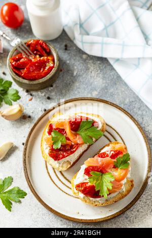 Offene Sandwiches oder Bruschetta mit gesalzenem Lachs, Käse und sonnengetrockneten Tomaten auf einem Steintisch. Gesundes Essen, Meeresfrüchte. Stockfoto