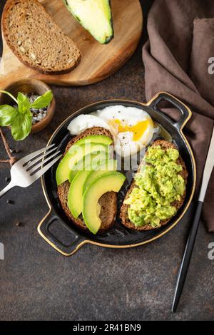 Vollkornbrot, Avocado in Scheiben und pochiertes Ei auf Steinhintergrund. Gesundes Frühstückskonzept, Sandwich mit Avocado und Stockfoto