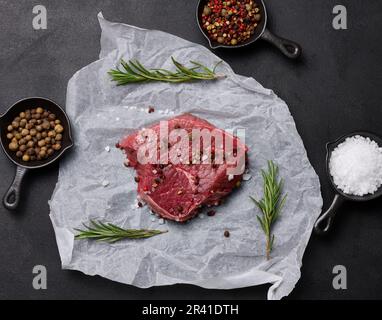 Rohes Rindfleisch mit Gewürzen liegt auf einem weißen Stück Pergamentpapier, Draufsicht Stockfoto