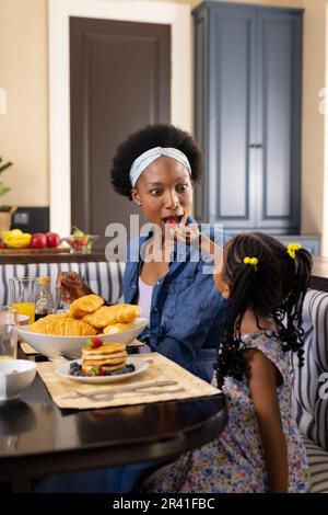 Ein afroamerikanisches Mädchen füttert die Mutter mit Erdbeeren, während es zu Hause am Esstisch frühstückt Stockfoto