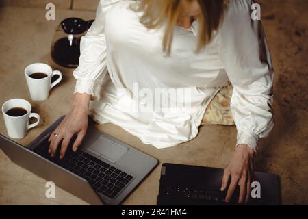 Frau mit Kaffeetassen vor zwei Laptops. Deadline, Nacharbeit, Multitasking, Fleiß-Freelancer-Konzept. Stockfoto