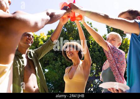 Fröhliche, vielfältige Gruppe von Freunden, die im Garten anstoßen Stockfoto