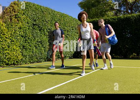 Glückliche, vielfältige Gruppe von Freunden, die zusammen auf dem Tennisplatz ankommen Stockfoto