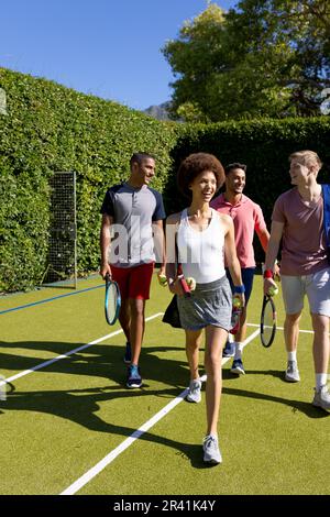 Glückliche, vielfältige Gruppe von Freunden, die zusammen auf dem Tennisplatz ankommen Stockfoto