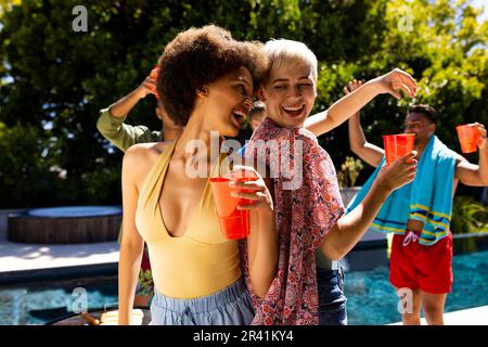 Fröhliche, vielfältige Gruppe von Freunden, die eine Poolparty veranstaltet und im Garten tanzt Stockfoto