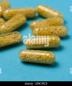 Transparente medizinische Kapseln mit gelbem Granulat innen auf blauem Hintergrund, Tabletten zur Behandlung, Vitamine Stockfoto