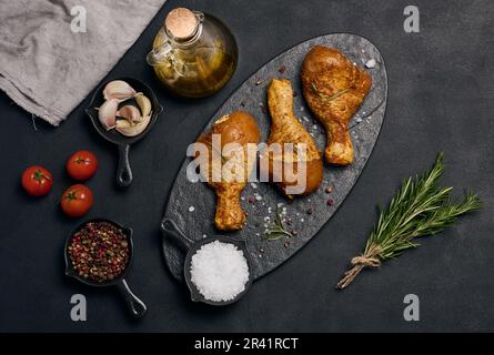 Rohe Hühnerschenkel in Gewürzen auf einem schwarzen Brett, Draufsicht. Mit Gewürzen kochen Stockfoto