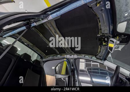 Rolle von Schallschutzmaterial zu Autoteilen. Die Installation der Schalldämmung des Fahrzeugs. Arbeiter klebt schallisolierendes Material auf die Innenseite des Stockfoto