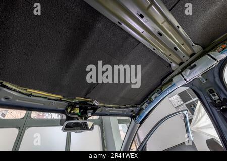 Rolle von Schallschutzmaterial zu Autoteilen. Die Installation der Schalldämmung des Fahrzeugs. Arbeiter klebt schallisolierendes Material auf die Innenseite des Stockfoto