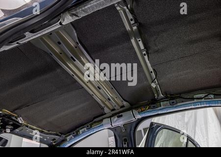 Rolle von Schallschutzmaterial zu Autoteilen. Die Installation der Schalldämmung des Fahrzeugs. Arbeiter klebt schallisolierendes Material auf die Innenseite des Stockfoto