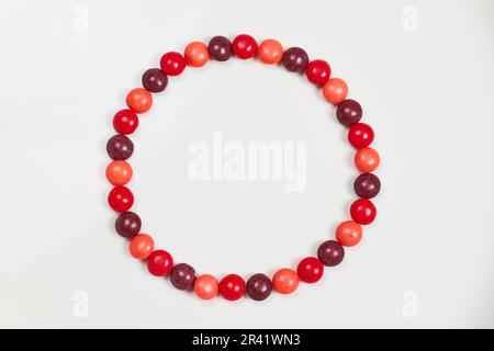 Ring aus kittelförmigen Süßigkeiten in einem Kreis auf weißem Hintergrund und verschiedene Valentinstag-Farben in Purpurrot und Pink Stockfoto