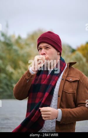 Lateinischer junger Mann, der im Winter über seine Hand hustet. Kaltes Wetter. Grippe. Stockfoto