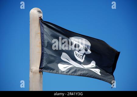 Piratenflagge mit Schädel und Kreuzknochen, die gegen den blauen Himmel fliegen Stockfoto