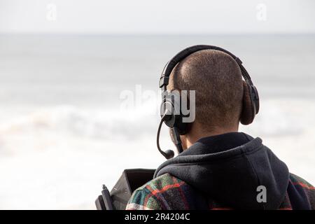 Kameramann mit Headset-Filmen am Strand Stockfoto