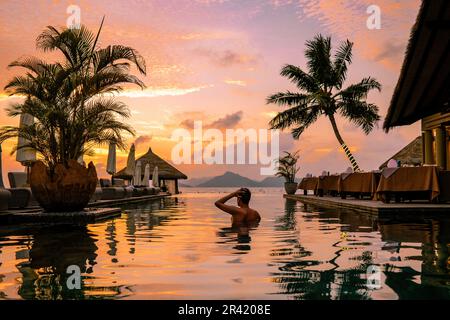 Luxuriöses Schwimmbad im tropischen Resort, entspannender Urlaub auf den Inseln der Seychellen. La Digue, Junger Mann bei Sonnenuntergang über der Schwimmhalle Stockfoto