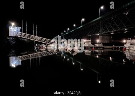 Boote legten nachts unter einer Brücke an, mit Reflektionen auf dem Wasser Stockfoto