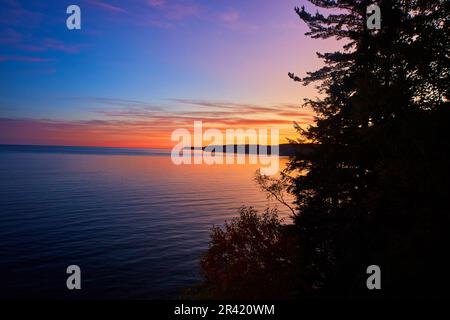 Sonnenuntergang Gold über einem großen See mit einer Silhouette aus Kiefern und einer entfernten Halbinsel Stockfoto